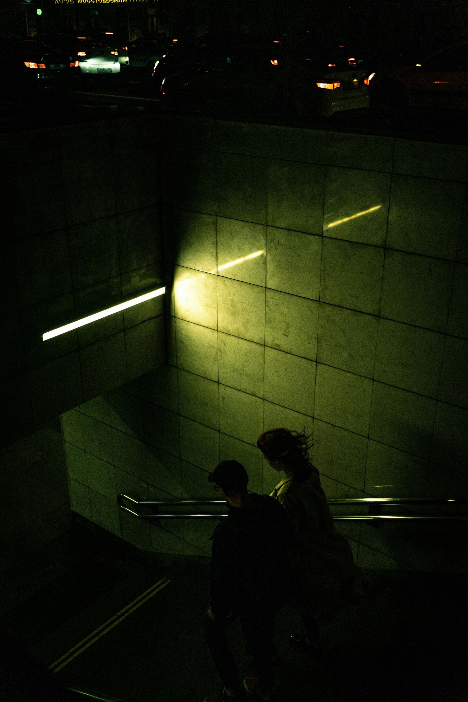 A couple descends into a dimly lit subway entrance, capturing urban nightlife.